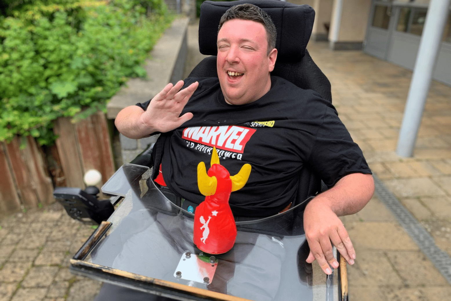 Service User Male Wheelchair User smiling and waving in a courtyard